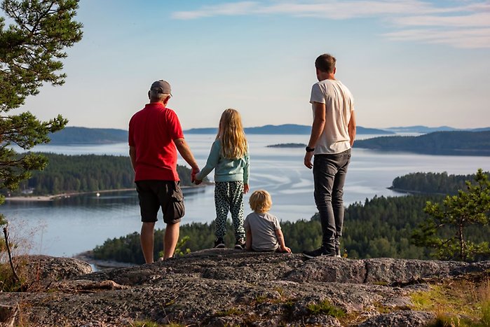 Naturvy från ett berg med två vuxna och två barn som står med ryggen mot kameran och blickar ut över ett hav.