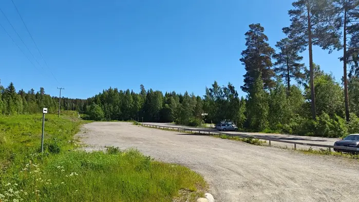 Grusparkering omgiven av grönska, blå himmel och två bilar står parkerade.