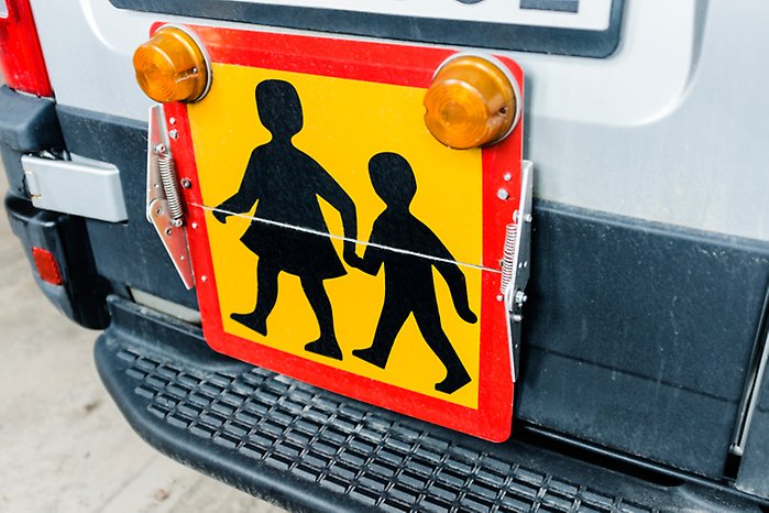 Skylt för skolskjuts på ett fordon, en orange platta med röd ram och svarta siluetter på ett stort och ett litet barn. 