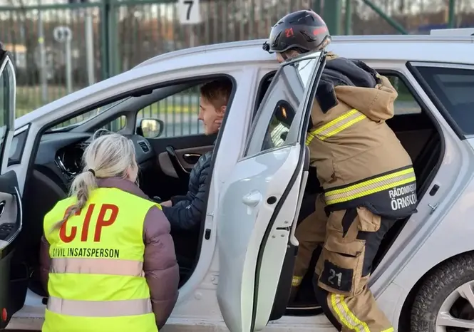 Brandman och frivillig hjälper person i bil under övning.