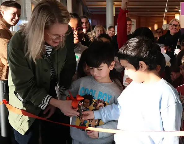 En vuxen och två skolelever klipper band